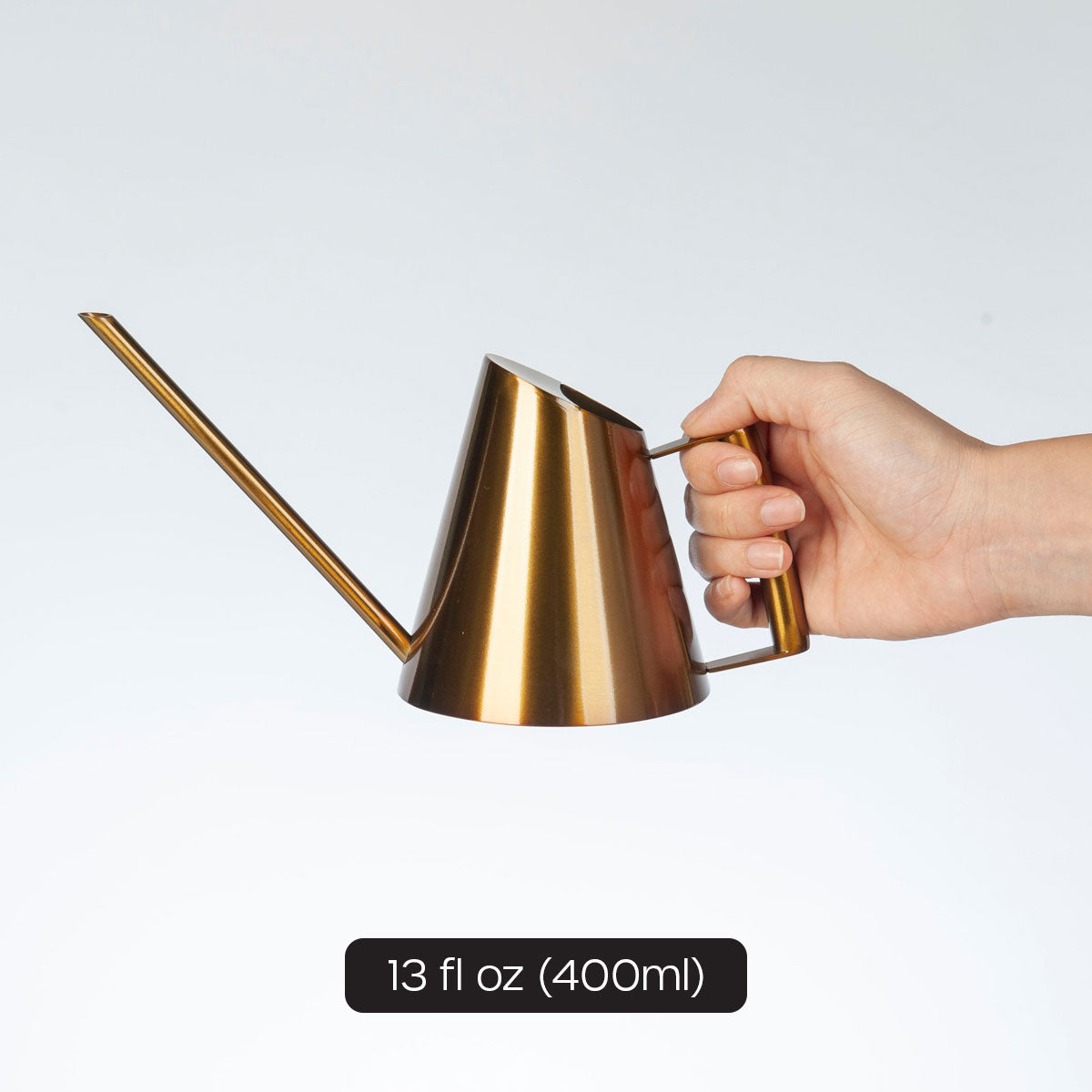 female hand model holding gold mini watering can showing 13 fl oz volume.
